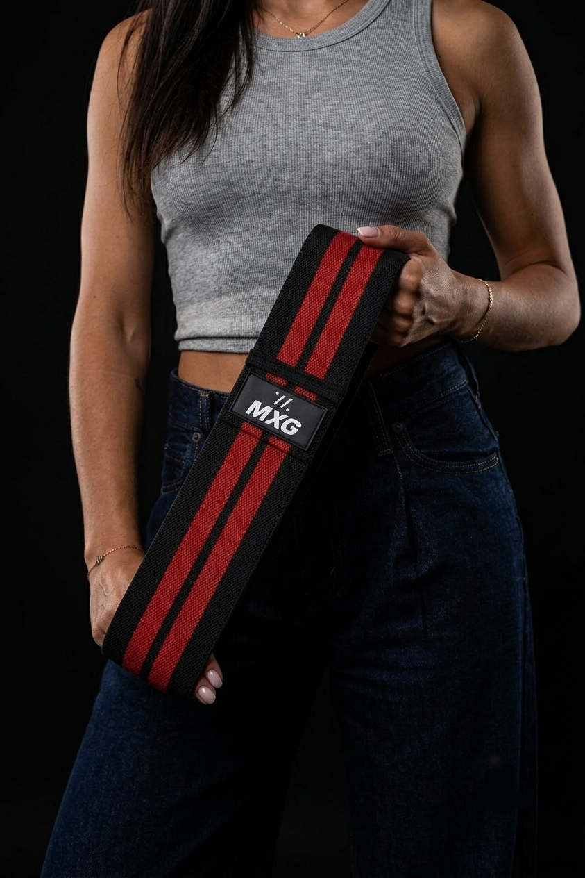 "Woman in a gray crop top and dark jeans holding a black and red striped wrist wrap against a black background"
